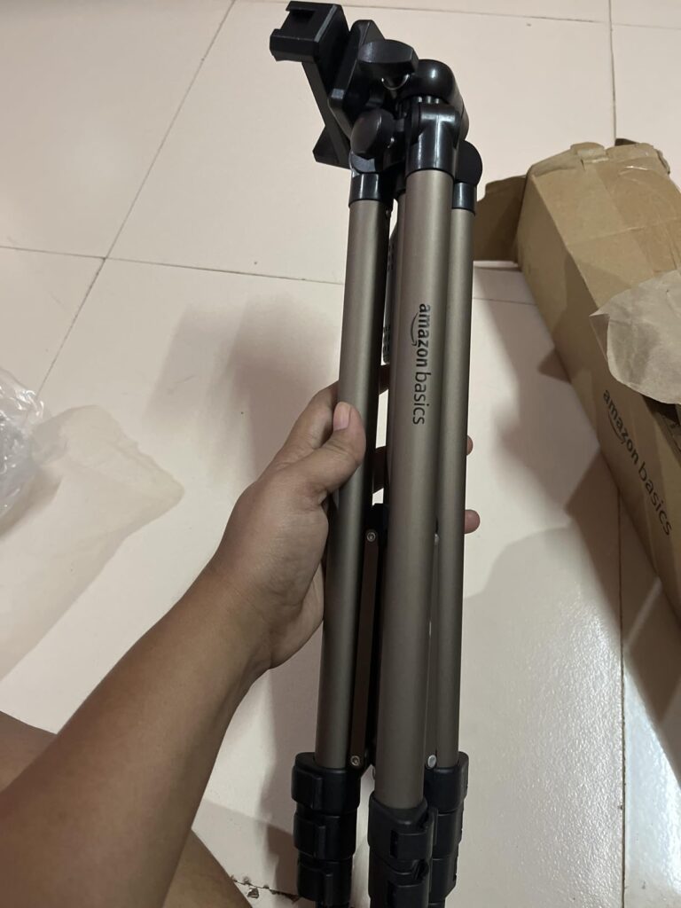 Folded Amazon Basics aluminium tripod under 1000 held in hand showing compact portable design for mobile photography and vlogging