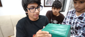 A young men and a kid (Sourav Joshi and Kunali) hold a green box while unboxing a Rolex watch, showcasing excitement and anticipation.