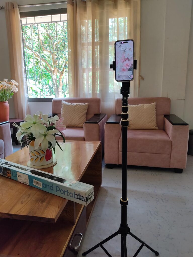 Mobile phone mounted on a tall tripod stand in living room setup for vlogging and YouTube recording
