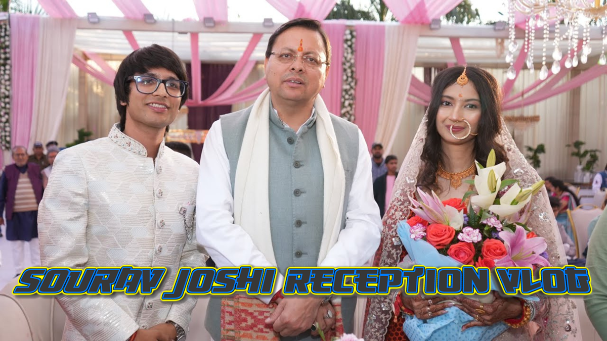 Three people (Sourav Joshi, sourav joshi wife and, Pushkar Singh Dhami, ) pose at an event under pink and white drapes. A man in glasses smiles, another wears a traditional suit, and a sourav joshi's wife (avantika bhatt) holds a bouquet, looking delighted.