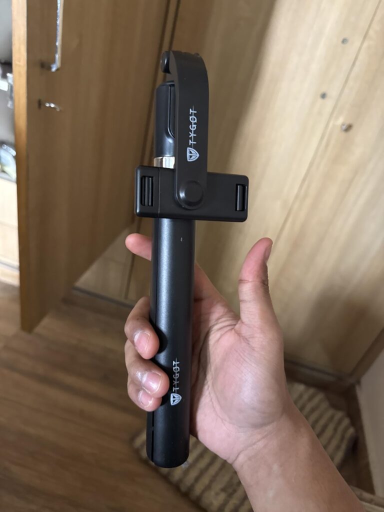Hand holding Tygot T9 3-in-1 selfie stick tripod in folded mode showing clamp and compact portable design